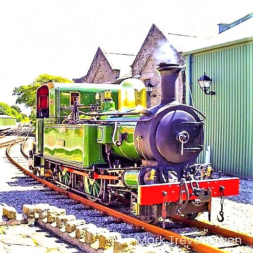 A bright green steam engine sitting on the railway tracks. 