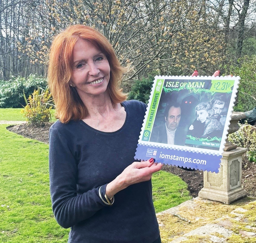 Jane Asher, both holding, and appearing on, a giant Manx stamp. 